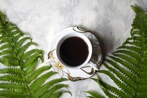 Matin café dans ancien tasse et feuilles de fougère sur une table Haut voir. photo