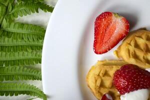 gaufres avec fraise sur une plaque, vert feuilles de fougère sur une tableau. proche en haut. magnifique et savoureux petit déjeuner. photo