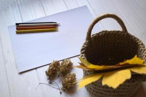 blanc papier, multicolore des crayons et l'automne feuilles dans une panier sur le bureau. photo