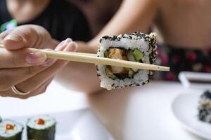 femme est en portant Sushi rouleau dans bambou des bâtons. photo