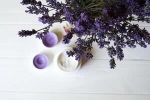 lavande fleurs, bougies et crème sur une blanc en bois Contexte. beauté se soucier. Haut voir. photo