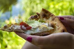 une pièce de Pizza dans le mains de une femme, proche en haut. photo