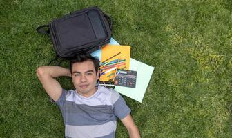 une Masculin étudiant mensonge sur le herbe avec une sac à dos et une calculatrice photo