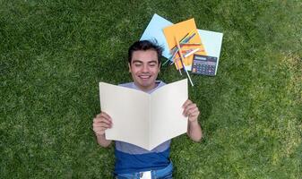 une Masculin étudiant mensonge sur le herbe en train de lire une document photo