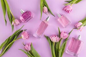 une ensemble de parfum bouteilles de divers formes sur une lilas Contexte avec délicat rose tulipes. plat poser. Haut voir. présentation de printemps parfums photo