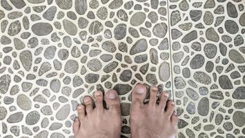 une yeux d'oiseau vue de bronzé Humain pieds permanent sur uniquement en forme de cendre carrelage dans une salle de bains avec l'eau éclabousser et fonctionnement vers le bas le drainer. photo