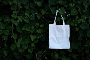 Sac fourre-tout en tissu blanc vierge à l'arrière-plan du feuillage des arbres de brousse verte photo