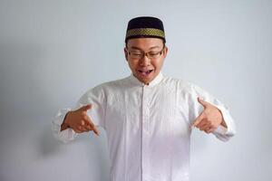 asiatique musulman homme portant des lunettes et blanc tissu montrer du doigt vers le bas pose pour ramadhan et eid Al fitr. isolé blanc Contexte photo
