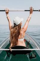 femme dans kayak retour voir. content Jeune femme avec longue cheveux flottant dans transparent kayak sur le cristal clair mer. été vacances vacances et de bonne humeur femelle gens relaxant ayant amusement sur le bateau photo