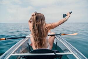 femme dans kayak retour voir. content Jeune femme avec longue cheveux flottant dans transparent kayak sur le cristal clair mer. été vacances vacances et de bonne humeur femelle gens relaxant ayant amusement sur le bateau photo