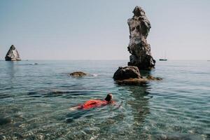 femme Voyage mer. content touristique dans rouge robe prendre plaisir prise image en plein air pour souvenirs. femme voyageur posant dans mer plage, entouré par volcanique montagnes, partage Voyage aventure périple photo