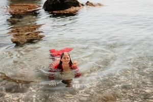 femme Voyage mer. content touristique dans rouge robe prendre plaisir prise image en plein air pour souvenirs. femme voyageur posant dans mer plage, entouré par volcanique montagnes, partage Voyage aventure périple photo