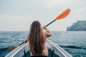 femme dans kayak retour voir. content Jeune femme avec longue cheveux flottant dans transparent kayak sur le cristal clair mer. été vacances vacances et de bonne humeur femelle gens relaxant ayant amusement sur le bateau photo