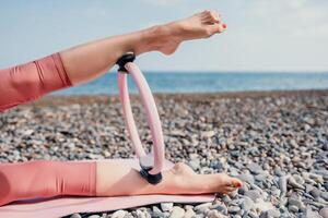 femme mer pilates. sportif content milieu vieilli femme pratiquant aptitude sur plage près mer, souriant actif femelle formation avec bague sur yoga tapis dehors, profiter en bonne santé mode de vie, harmonie et méditation photo