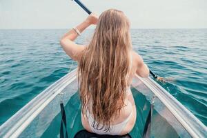 femme dans kayak retour voir. content Jeune femme avec longue cheveux flottant dans transparent kayak sur le cristal clair mer. été vacances vacances et de bonne humeur femelle gens relaxant ayant amusement sur le bateau photo