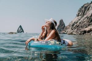 femme été mer. content femme nager avec gonflable Donut sur le plage dans été ensoleillé jour, entouré par volcanique montagnes. été vacances concept. photo