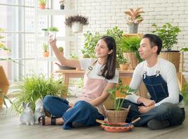 portrait Jeune asiatique couple portant un tablier elles ou ils sont portion à organiser une petit arbre dans une arbre tronc sur une en bois table dans leur maison. à embellir avec le brillant et content sourire de le couple photo