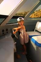 portrait de une mignonne caucasien fille, portant été robe et une capitaine casquette, conduite une yacht photo