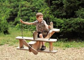 cinq année vieux garçon en volant sur une en bois biplan balançoire dans le été parc photo