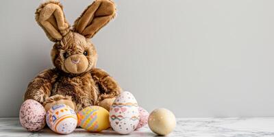 ai généré une photo avec une peluche marron lapin jouet avec longue oreilles séance dans de face de une rangée de coloré peint des œufs. le lapin apparaît mignonne et duveteux contre le vibrant toile de fond de le des œufs