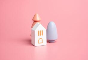 maison et coloré des arbres sur une rose Contexte. en bois figurines jouets. acheter une maison. bien logement. hypothèque. confortable et doux tons. pastel rose couleurs. photo