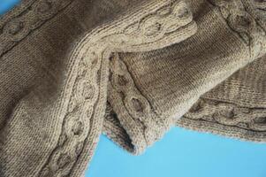 en tissu de une beige la laine tricoté écharpe sur une bleu Contexte. Fait main hiver accessoires. photo