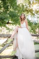 magnifique fille dans blanc robe avec une couronne de fleurs sur sa tête est permanent Extérieur dans le parc avec vert feuille sur le Contexte photo