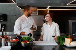 Beau Jeune africain chef est cuisine ensemble avec le sien caucasien petite amie dans le cuisine en utilisant rouge du vin comme un ingrédient. photo