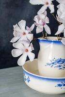 branche de délicat rose magnolia fleur dans plein Floraison dans ancien céramique cruche pour la lessive sur foncé Contexte photo