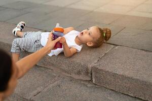 une peu caucasien fille mensonges sur sol dans ville tire le sien main derrière Plastique bouteille. photo
