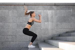 Urbain sportif femme entraînement. femelle athlète Faire s'accroupir sauts sur Urbain escaliers. photo