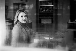 Jeune femme dans café avec tasse, Jeune fille à l'extérieur fenêtre - Candide moment dans café capturé dans noir et blanc - contraste de intérieur et Extérieur réglages dans café scène. photo