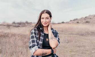 content Jeune souriant femme avec taches de rousseur en plein air portrait. doux ensoleillé couleurs. Extérieur fermer portrait de une Jeune brunette femme et à la recherche à le caméra, posant contre l'automne la nature Contexte photo