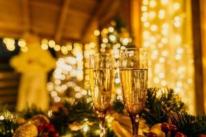 deux Champagne des lunettes rempli avec Champagne sont mis sur une table près à Noël arbre. le des lunettes sont entouré par lumières, création une de fête atmosphère. photo