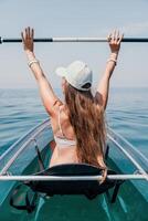 femme dans kayak retour voir. content Jeune femme avec longue cheveux flottant dans transparent kayak sur le cristal clair mer. été vacances vacances et de bonne humeur femelle gens relaxant ayant amusement sur le bateau photo