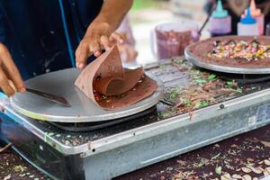 fabrication de crêpes Crêpes avec Chocolat et Chocolat riz dans ouvert marché Festival équitable. une main est fabrication crêpes en plein air sur une métal plaque photo