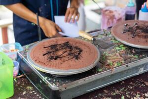 fabrication de crêpes Crêpes avec Chocolat et Chocolat riz dans ouvert marché Festival équitable. une main est fabrication crêpes en plein air sur une métal plaque photo