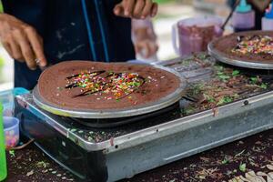 fabrication de crêpes Crêpes avec Chocolat et Chocolat riz dans ouvert marché Festival équitable. une main est fabrication crêpes en plein air sur une métal plaque photo