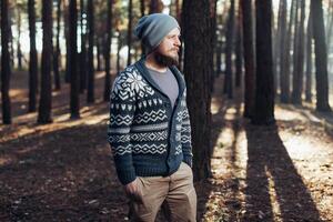 une Jeune homme avec une barbe des promenades dans une pin forêt. portrait de une brutal barbu homme l'automne forêt photo