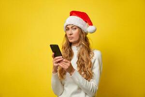 femme Noël Père Noël chapeau Jaune studio Contexte avec téléphone intelligent dans main photo