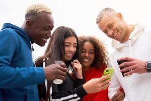 Jeune personnes, élèves de différent nationalités, sourire, tenir café dans leur main et Regardez dans un téléphone intelligent. dépenser temps ensemble avec amis. deux Hommes et deux femmes. blanc Contexte. photo