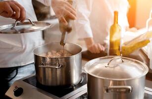 fermer mains de chef verser du vin dans pot avec Viande. dans le Contexte est une flou figure de un autre chef photo