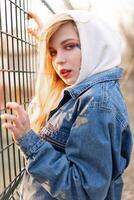 Jeune femme avec temporaire peint fleurs sur le affronter. adolescent fille avec longue blond cheveux porter jeans veste et sweat à capuche photo