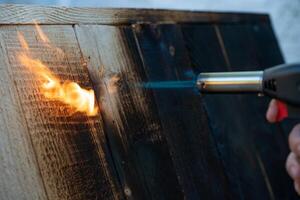 professionnel Charpentier en utilisant vieux traditionnel Japonais technique. brûlant bois planches avec gaz brûleur photo
