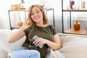 Enceinte femme Ecoutez la musique écouteurs mensonge sur le canapé en portant téléphone intelligent dans main photo