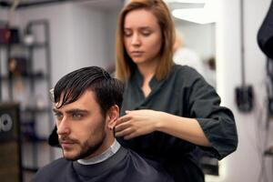 Beau bleu regardé homme séance dans coiffeur magasin. coiffeur coiffeur femme Coupe le sien cheveux. femelle coiffeur. photo