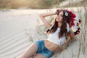 une magnifique Jeune caucasien fille dans une blanc Haut sur sa tête est portant un Indien chapeau. gardon est dans le désert. content vacances ambiance. photo