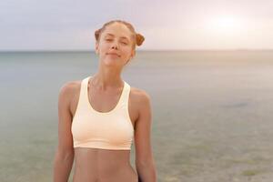 rafraîchissant sauvage mer côté entraînement. souriant en bonne santé aptitude femme dans des sports équipement sur le plage à la recherche dans le distance photo