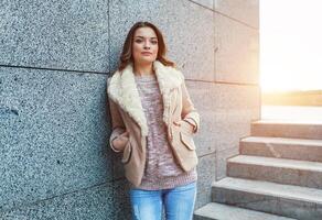 une magnifique Jeune brunette fille des promenades par le l'automne ville dans le des rayons de chaud lumière du soleil photo