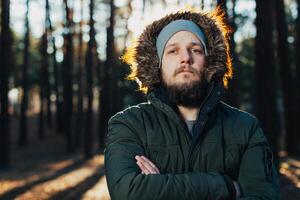 proche en haut portrait de une barbu branché touristique dans gris capuche homme dans le lumière du soleil photo